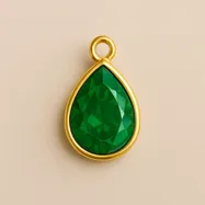 Gold-framed teardrop charm with a faceted emerald-green gemstone on a neutral background.